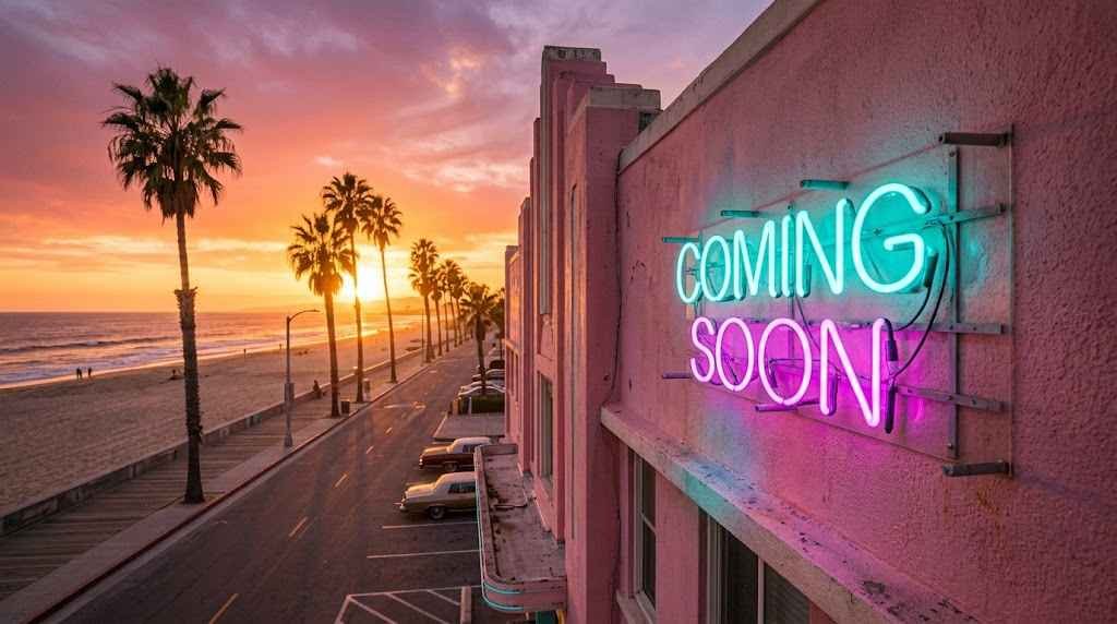A wide-angle, cinematic photograph of a retro neon sign reading "COMING SOON" in glowing cyan and magenta letters. The sign is mounted on a pink stucco building on a beachfront strip. The background shows tall palm trees, a sandy beach, and the ocean during a vibrant golden hour sunset with warm orange and purple hues in the sky.